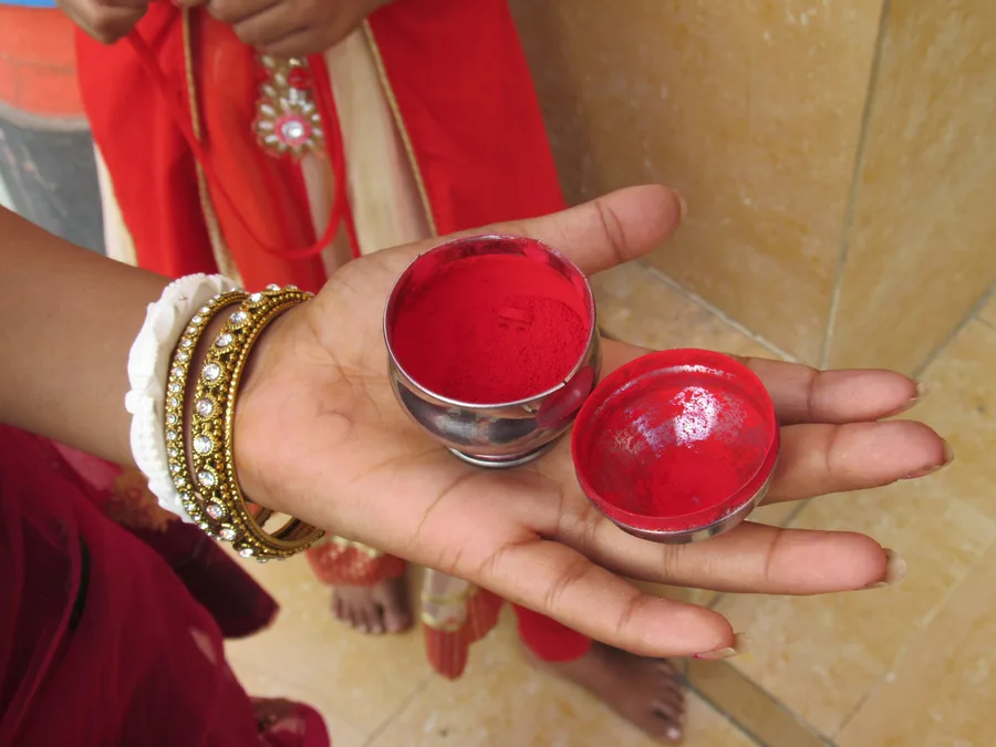 A devotee's hand holding small containers of red sindoor (vermillion) powder used in ritual offering.