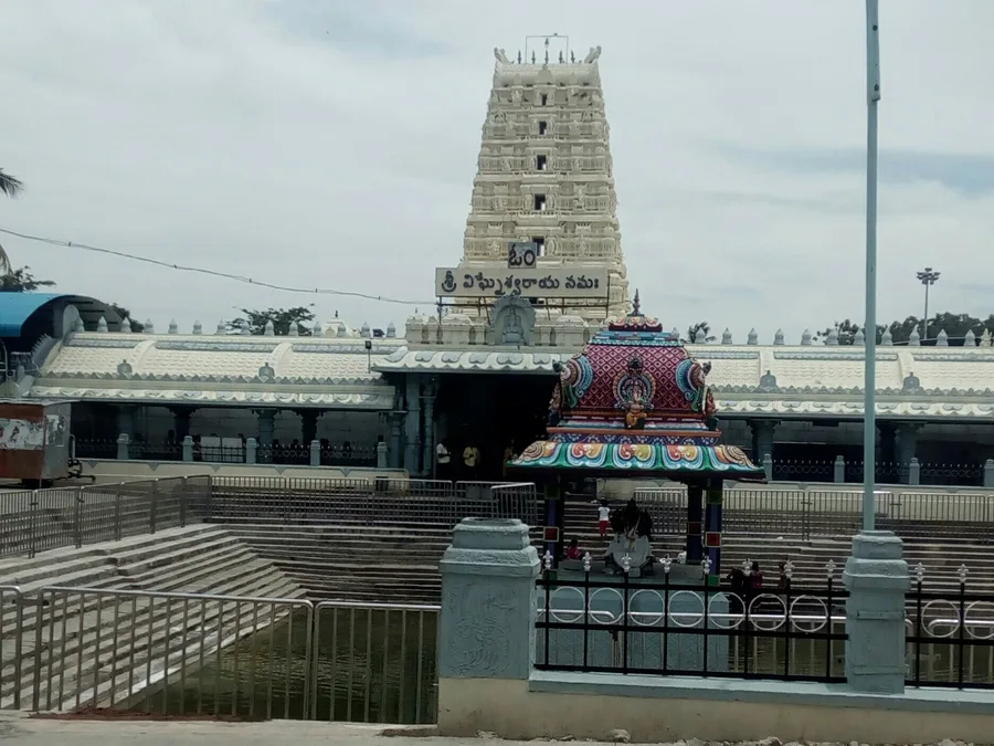 The ornate white gopuram of the Kanipakam Varasiddhi Vinayaka temple in Andhra Pradesh, seen beyond its sacred tank.