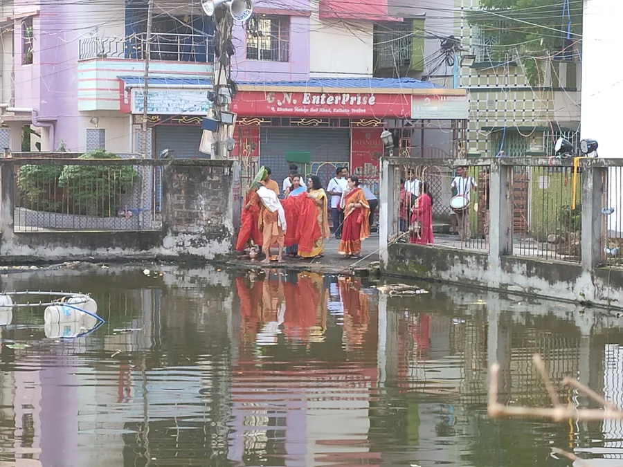 Devotees performing the Nabapatrika bathing ritual beside a pond during Durga Puja, part of the Kola Bou tradition.