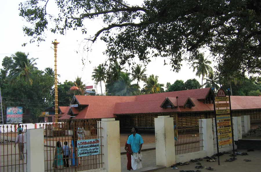 The red-tiled roof and courtyard of the Kottarakkara Sree Mahaganapathy temple in Kerala, shaded by a large tree.
