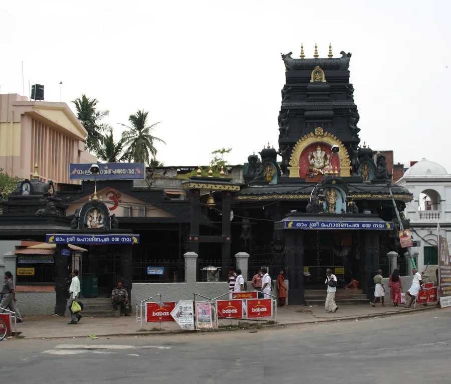 The dark stone tower of the Pazhavangadi Maha Ganapathy temple in Thiruvananthapuram, with a golden image of Ganesha set into its facade.