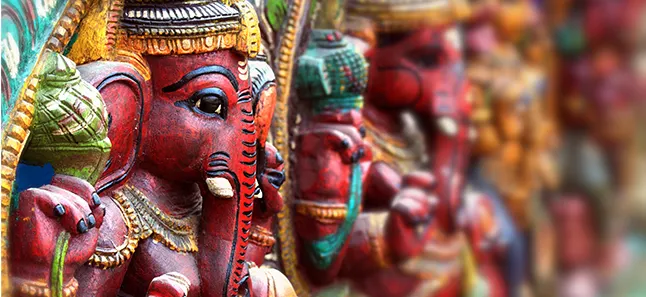A row of hand-carved wooden Ganesh masks in red, green, and gold, arranged in a receding line.