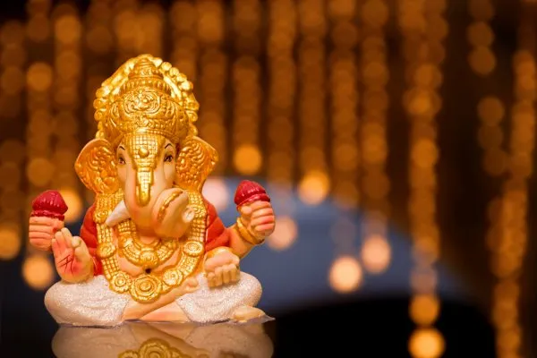 A small white marble Ganesh idol with gold accents, seated on a decorative plate ringed with colorful pom-poms.